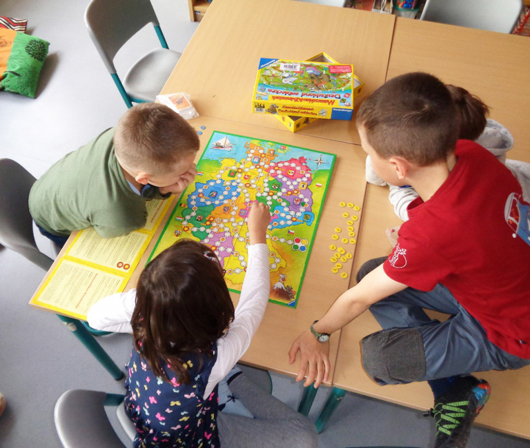 Vier Kinder spielen gemeinsam ein Gesellschaftsspiel an einem Tisch.