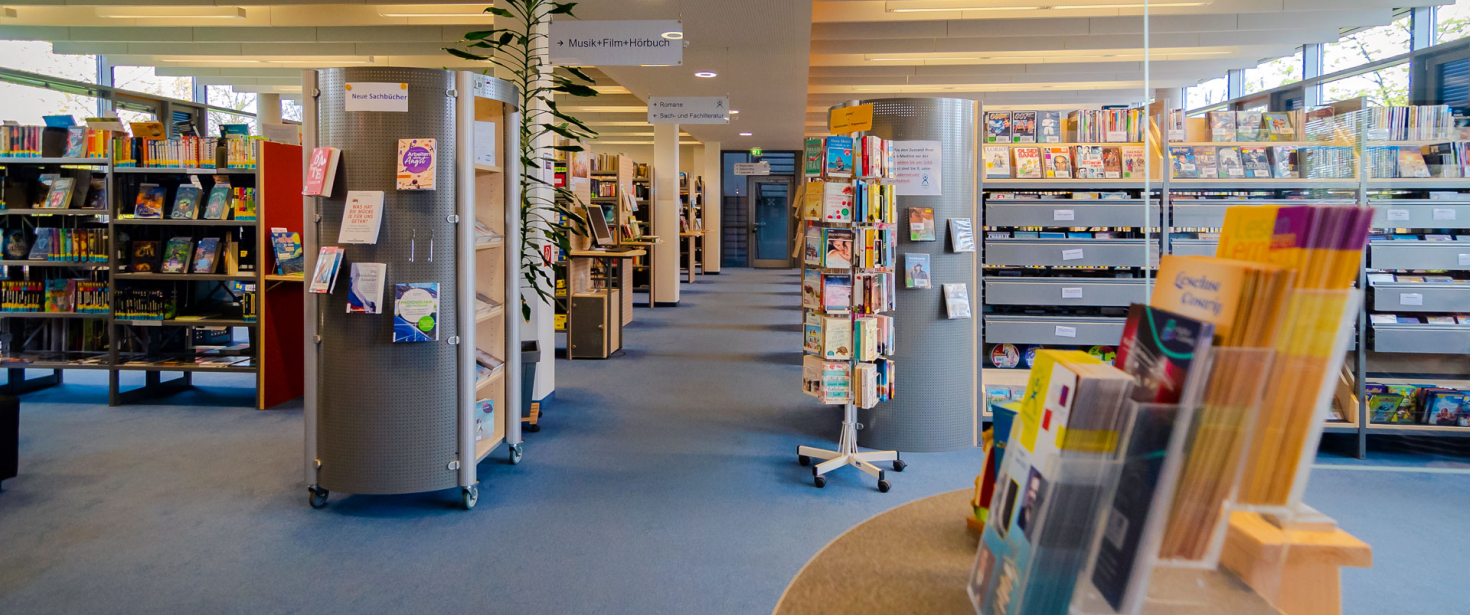 Blick auf den Mittelgang der Bibliothek, von Position der Servicetheke aus fotografiert. Im Hintergrund Bücherregale.