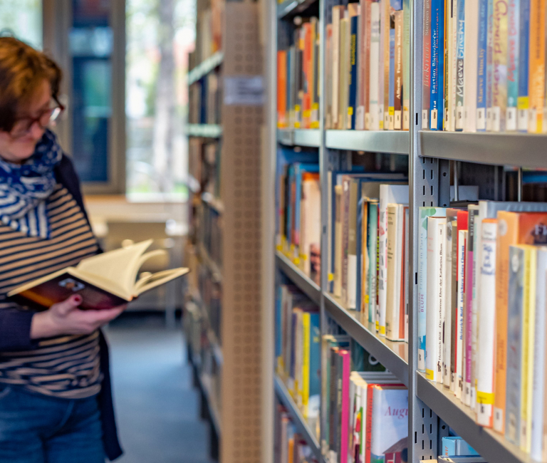 Eine Frau steht vor einem Bücherregal und blättert in einem Buch