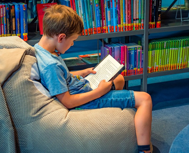 Junge sitzt auf einem Sitzsack in der Kinderabteilung und liest ein Buch.