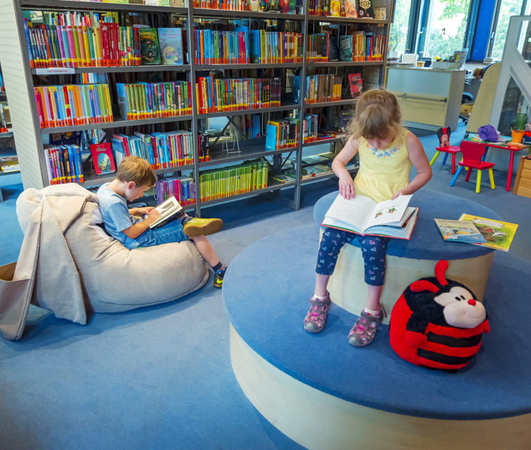 Ein Junge und ein Mädchen sitzen auf einem Sitzsack und dem Podest in der Kinderabteilung und lesen Bücher.