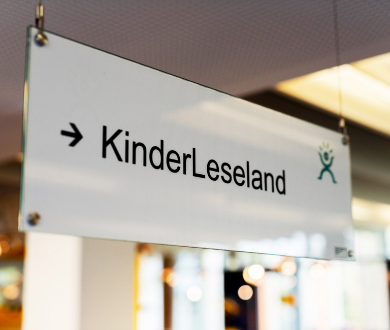 Von der Decke hängender Wegweiser zur Kinderabteilung mit dem Schriftzug ‚KinderLeseland‘
